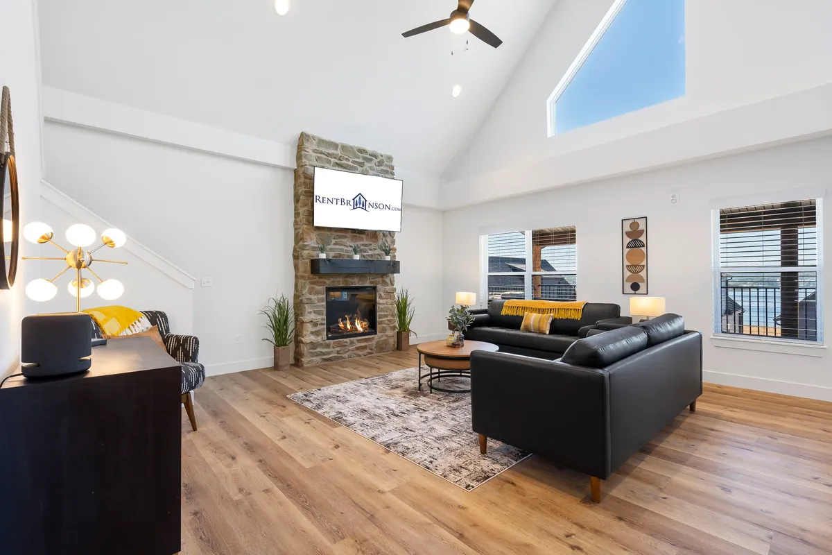 A stylish living room centered around a stone fireplace, with large windows, modern furniture, and soft lighting. The setup is ideal for cozying up, enjoying a movie, or simply relaxing while taking in lake views.