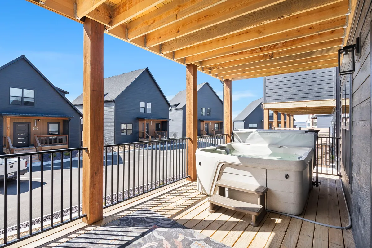 An exterior shot of the lower deck featuring a private hot tub with wooden decking, surrounded by adjacent homes and open sky above—ideal for unwinding or stargazing after a day of games.