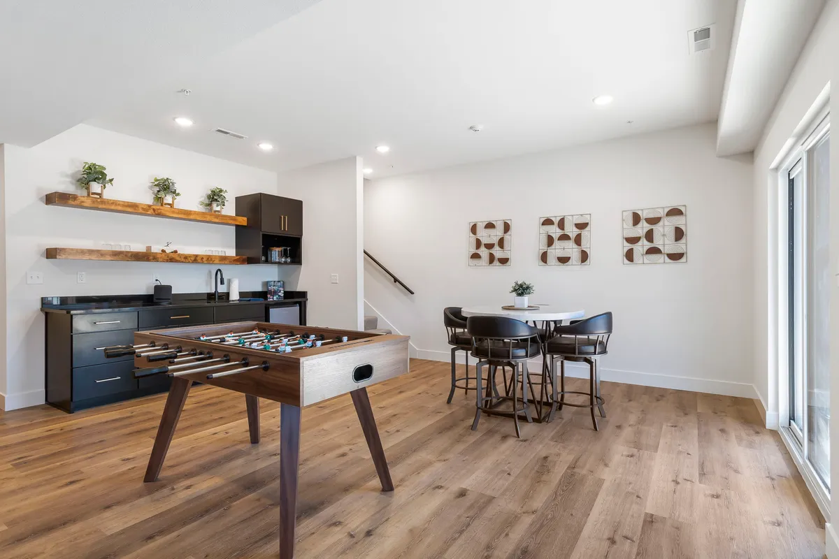 A fun and relaxed game area set up with a foosball table, a kitchenette for easy access to refreshments, a dining table for card games or meals, and cheerful wall art adding to the playful mood.