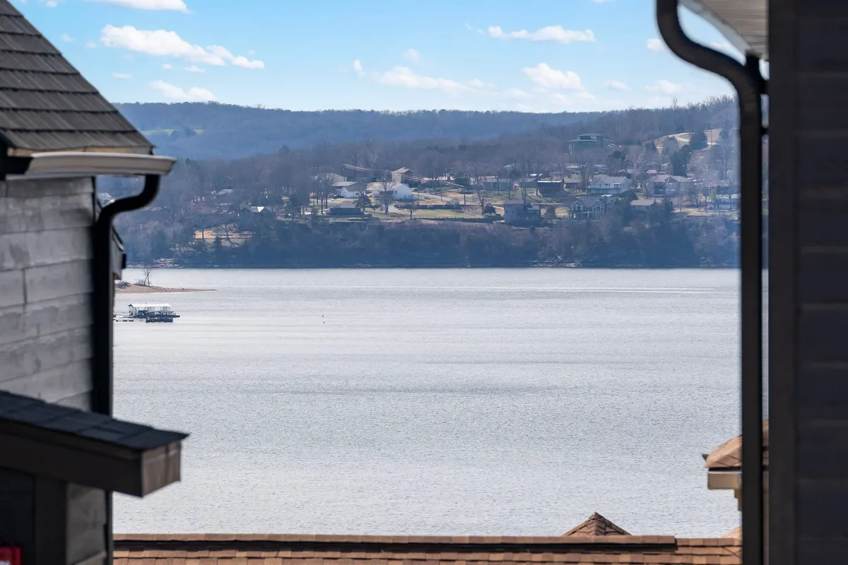 A picturesque vantage of Table Rock Lake with tranquil waters, distant houses, and rolling hills in the background. The soft light evokes early morning or sunset, ideal for quiet moments or photography from the deck.