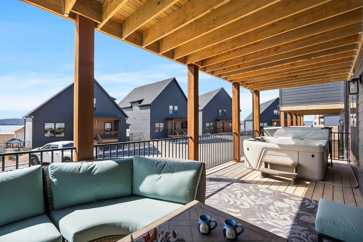 An outdoor hot tub and adjacent seating area overlook a scenic view of neighboring houses, suggesting a tranquil space perfect for group relaxation. The area is spacious enough for several people and features comfortable seating, with the soothing presence of water visible in the background.
