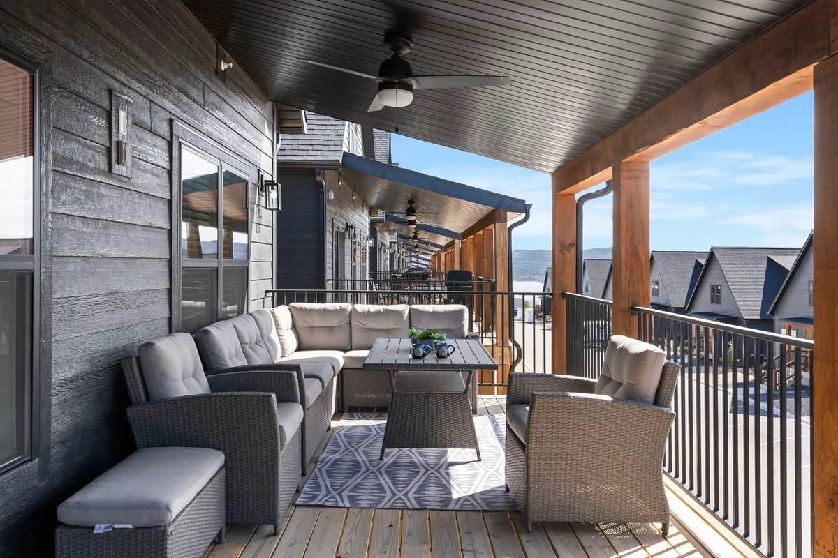 A spacious covered outdoor seating area is adorned with a decorative rug and wooden ceiling, with comfortable furniture arranged for socializing. Behind the seating, a mountain view provides a scenic backdrop, and the area feels welcoming for both people and pets.