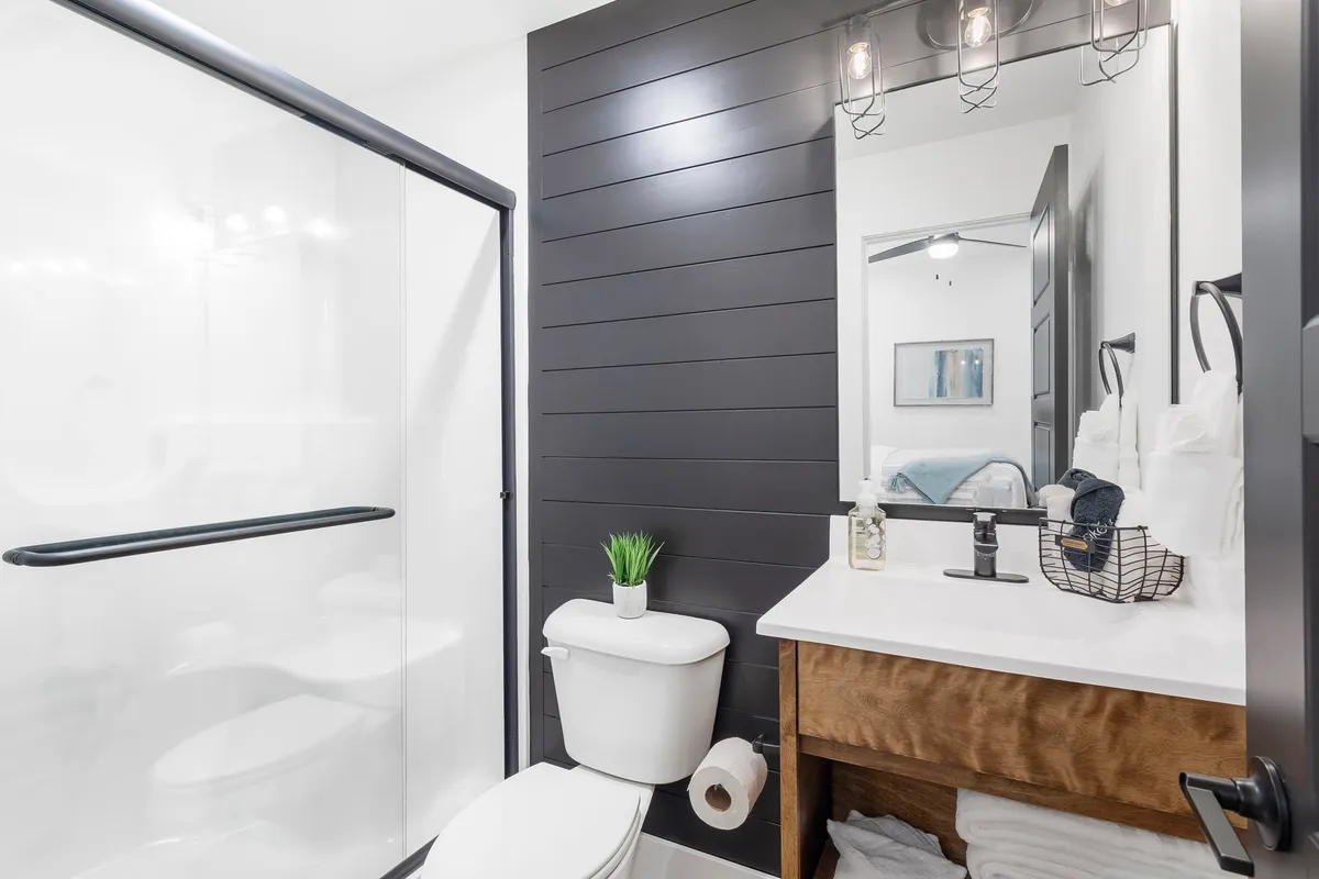 A modern bathroom featuring a bright shower area, a sleek vanity with a mirror above, and wooden cabinetry. The space feels fresh and spa-like, ideal for morning refreshment or evening relaxation.