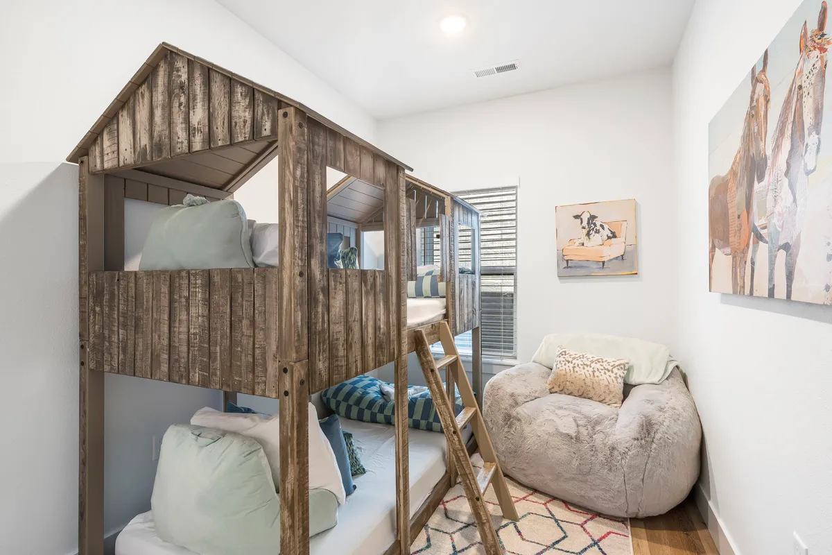 A fun and inviting bunk room, complete with a bunk bed, a bean bag chair for lounging or reading, and colorful wall art. The space is bright and cheerful, designed with children or young guests in mind.