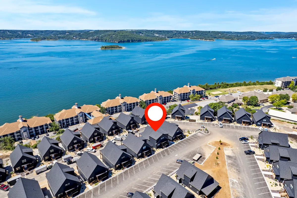 A relaxed lakeside scene showing Table Rock Lake with buildings along the water and a parking area, all bathed in the warm glow of sunset. The lake is the visual anchor, with space for boating and fishing, and the surrounding area hints at community events and water sports.